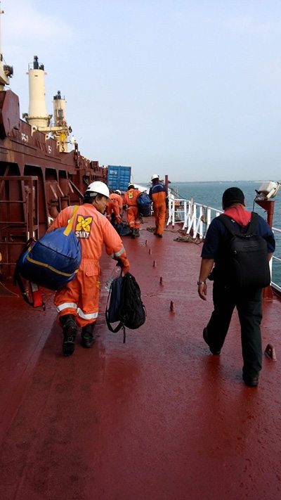 Seafarers carrying travel bags along a ship deck during a crew change