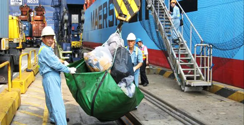 Workers guiding a crane sling filled with bagged ship waste onto the quay