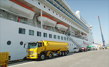 A yellow waste-oil collection tanker alongside a berthed cruise ship